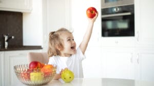 A little girl holds an apple in the air.