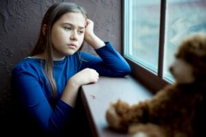 A little girl stands near a window and is feeling depressed.