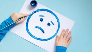 A child painting a sad face with blue paint.