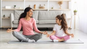 A mother and daughter meditate in the living room.
