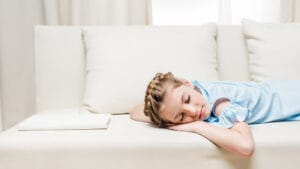 An adolescent girl sleeps on a couch.