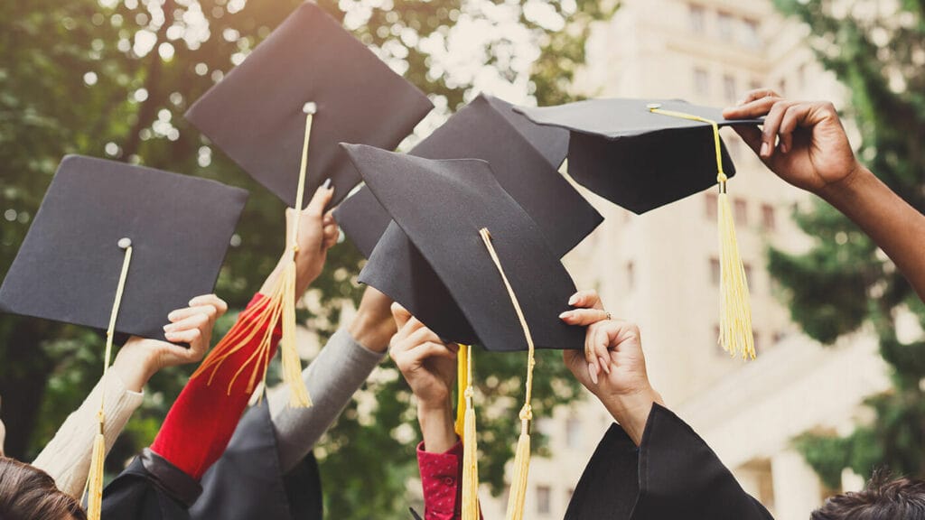 A group High School seniors raise their graduation caps towards the sky.
