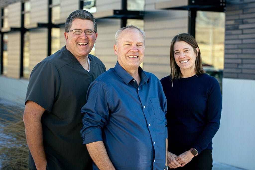 Steve, Brian, and Sadie smile outside the Stansbury Park office