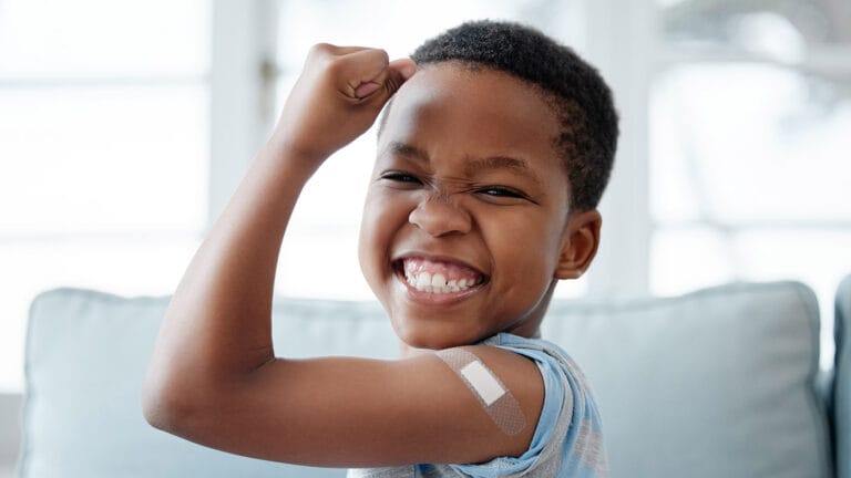 A boy smiling and flexing his arm after a vaccination.