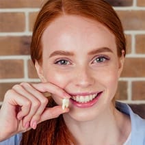 A teen smiling and holding their extracted tooth