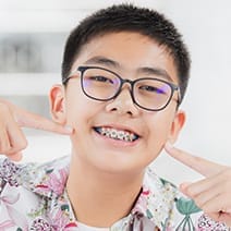 Teen smiles and points at braces on his teeth.