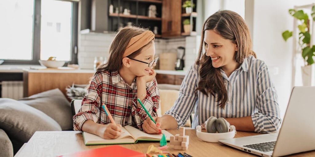 Mother and daughter working and smiling at kitchen table