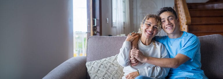 Teenage son hugging his mother on their living room couch