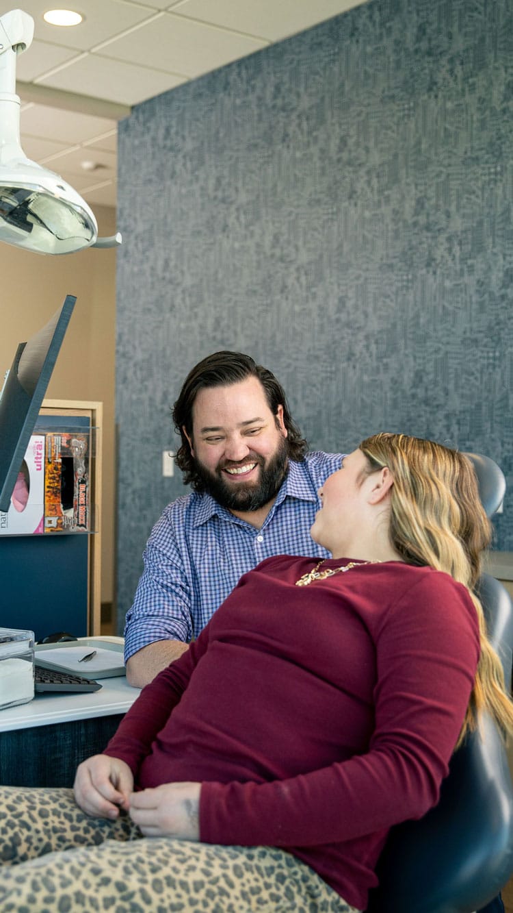 Orthodontist Dr. Casey Brewer smiles as he talks with a patient sitting in the orthodontic chair