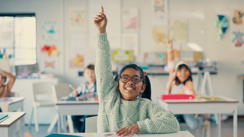 Excited young girl confidently raising her hand in the classroom