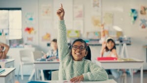 Excited young girl confidently raising her hand in the classroom