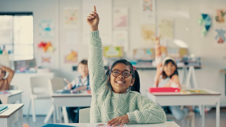 Excited young girl confidently raising her hand in the classroom