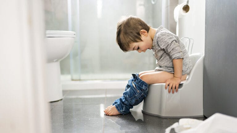 two year old boy sitting on a potty chair in the bathroom