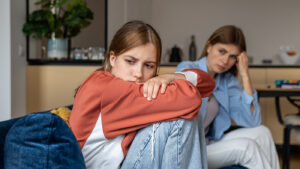 frustrated teen daughter sitting on the couch with her mom