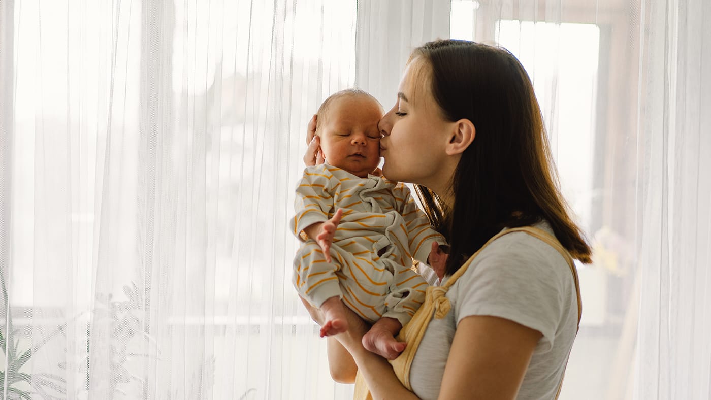 young mom holding newborn baby boy and kissing his cheeck