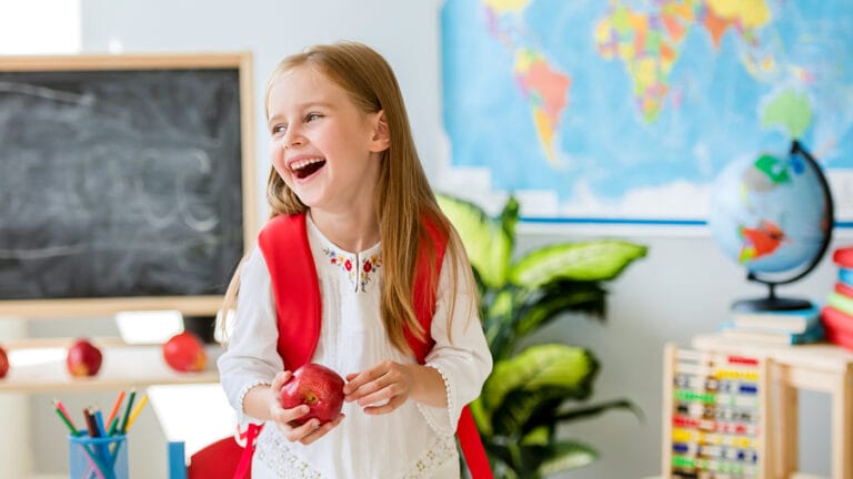 kindergartener in a school classroom holding an apple