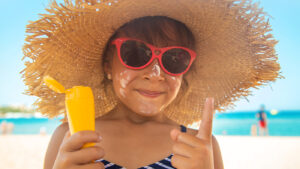 young girl wearing a sunhat and putting on sunscreen