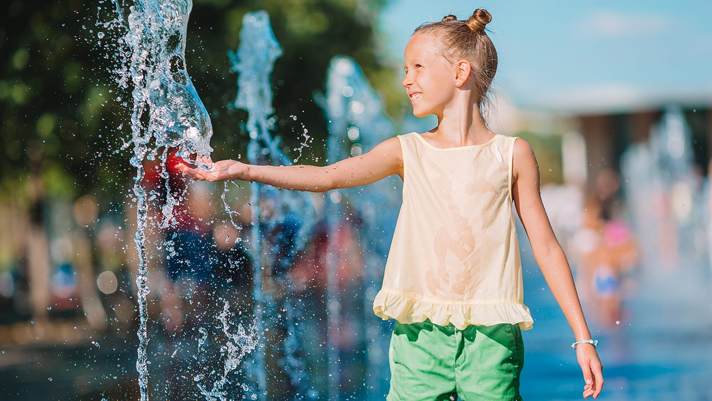 young girl playing in a splashpad fountain on a hot, summer day