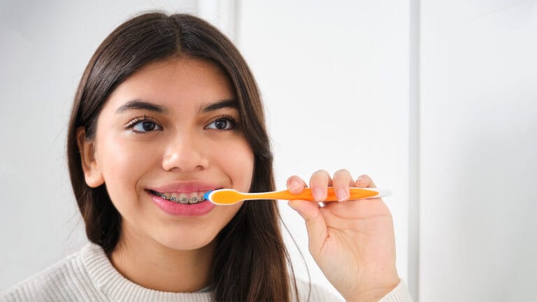 teen girl with braces brushing her teeth