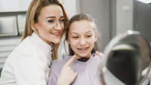 young girl looking at her new braces in the mirror at the orthodontist with the dental assistant