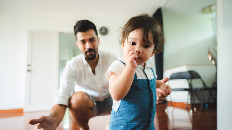 Young toddler sucking on thumbs while being called on by their dad
