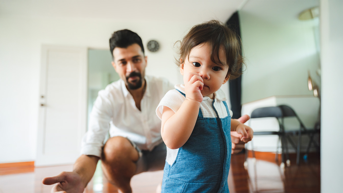 Young toddler sucking on thumbs while being called on by their dad