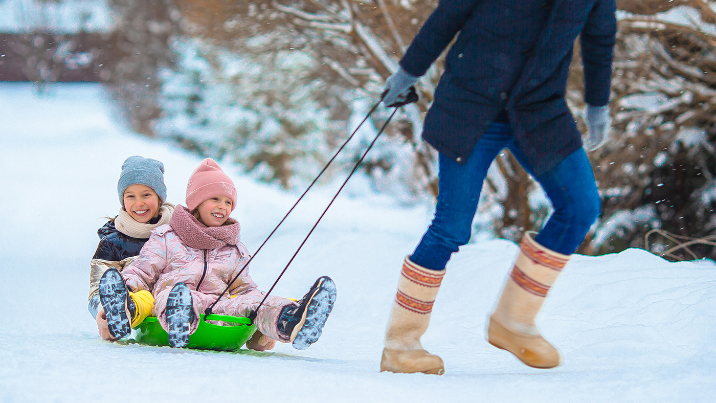 dad pulling two young girls on a sled in the snow