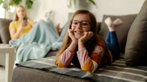 preteen girl hanging out on couch with her mom in the background