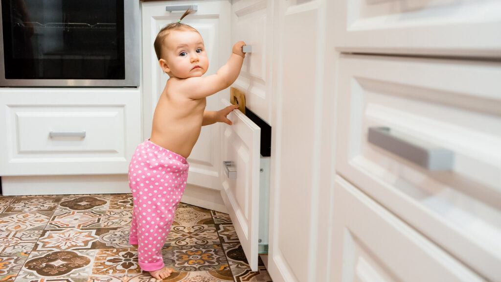 Young baby girl pulling on kitchen drawers at home