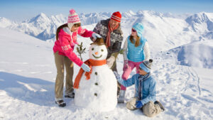 Family building a snowman together outside with mountains in the background