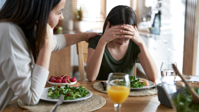 Mom consoling young tween daughter at dining table