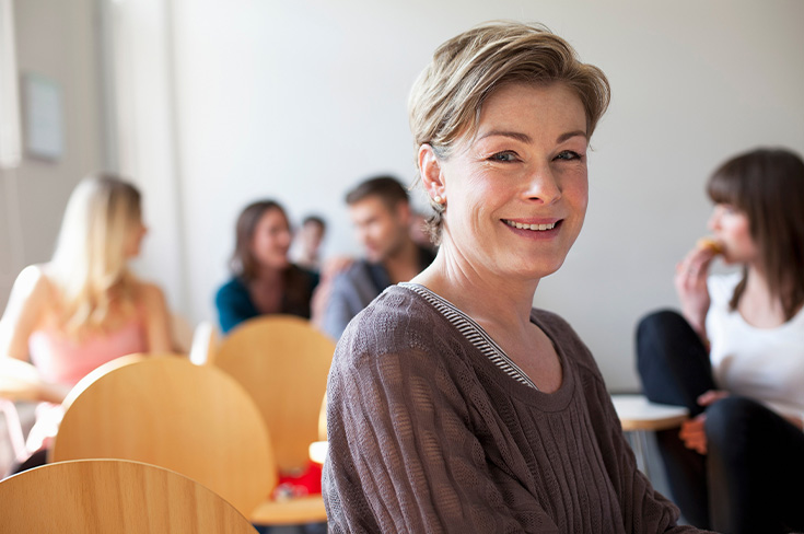Mother in a classroom smiling into the camera with other participants in the background