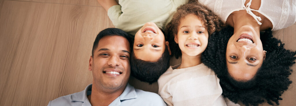 Family of four lying on wood floors smiling together