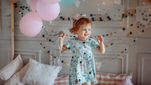 Girl toddler holding balloons and jumping on her bed