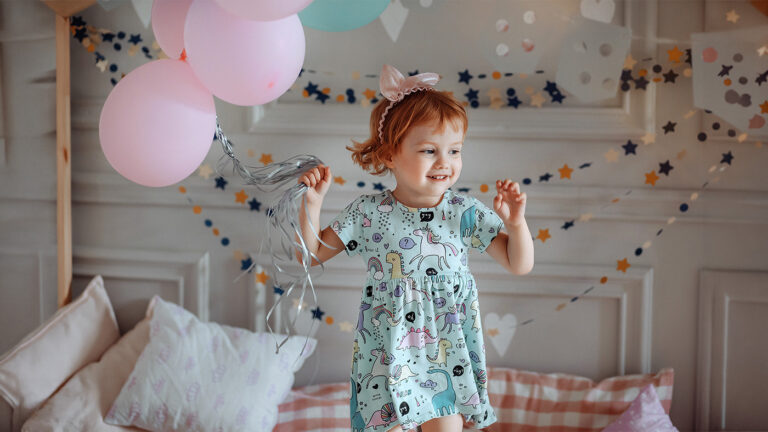 Girl toddler holding balloons and jumping on her bed