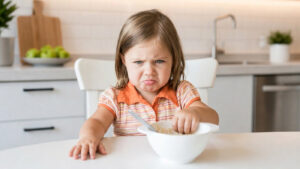 young girl making a face at her bowl of food
