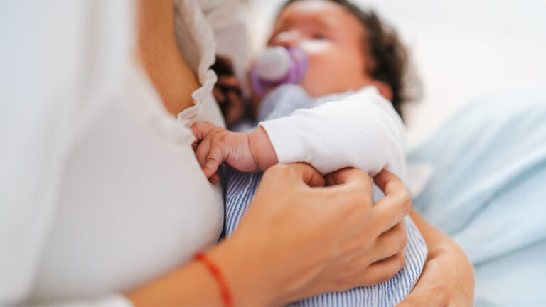 Newborn with a pacifier holding onto their mother