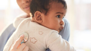 Young baby in an adult's arms getting a checkup with a stethoscope