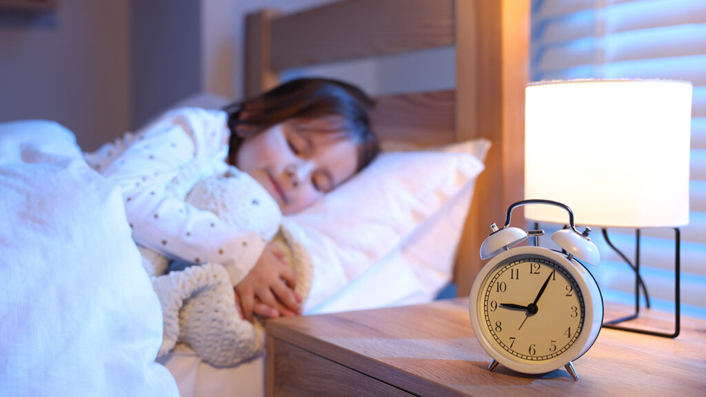 toddler sleeping in bed with a clock nearby