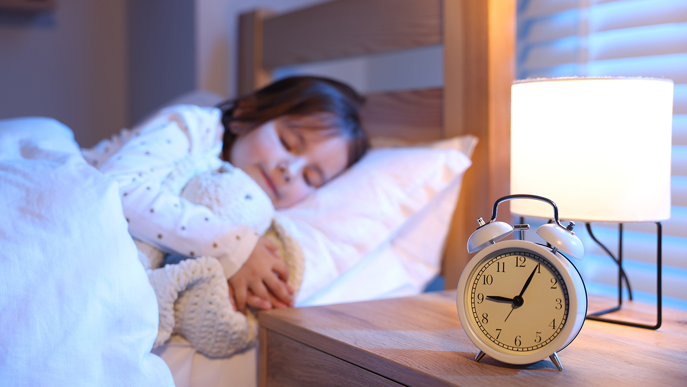 toddler sleeping in bed with a clock nearby