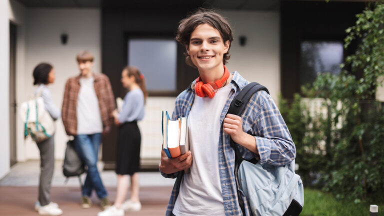 Young Freshman in college standing aside from his group of friends